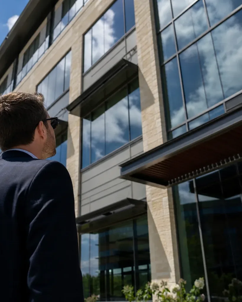 A property investor in business attire stands at the base of a glass-curtain-wall office tower in a North Austin tech